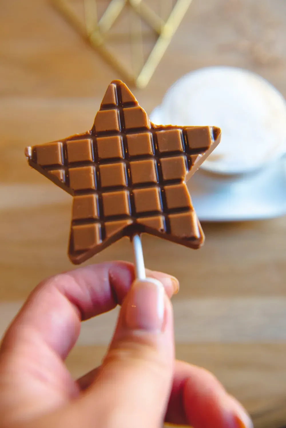 Acadea-stea din ciocolată cu caramel Choco Toni, ținută în mână lângă o ceașcă de cafea