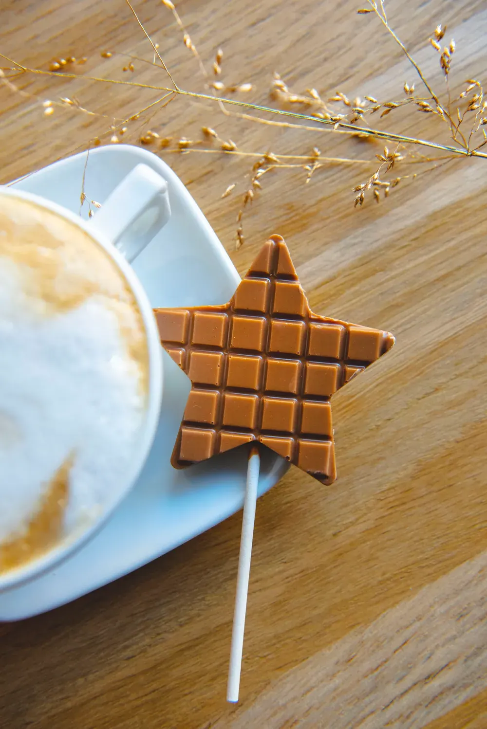 Acadea-stea din ciocolată cu caramel Choco Toni lângă un cappuccino, pe o masă de lemn
