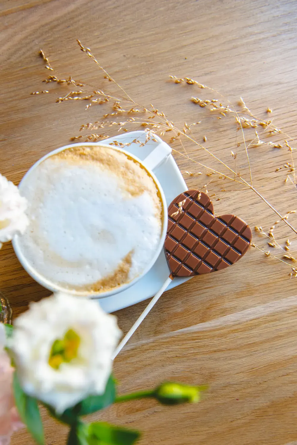 Acadea-inimă din ciocolată cu lapte Choco Toni lângă o cafea și flori albe