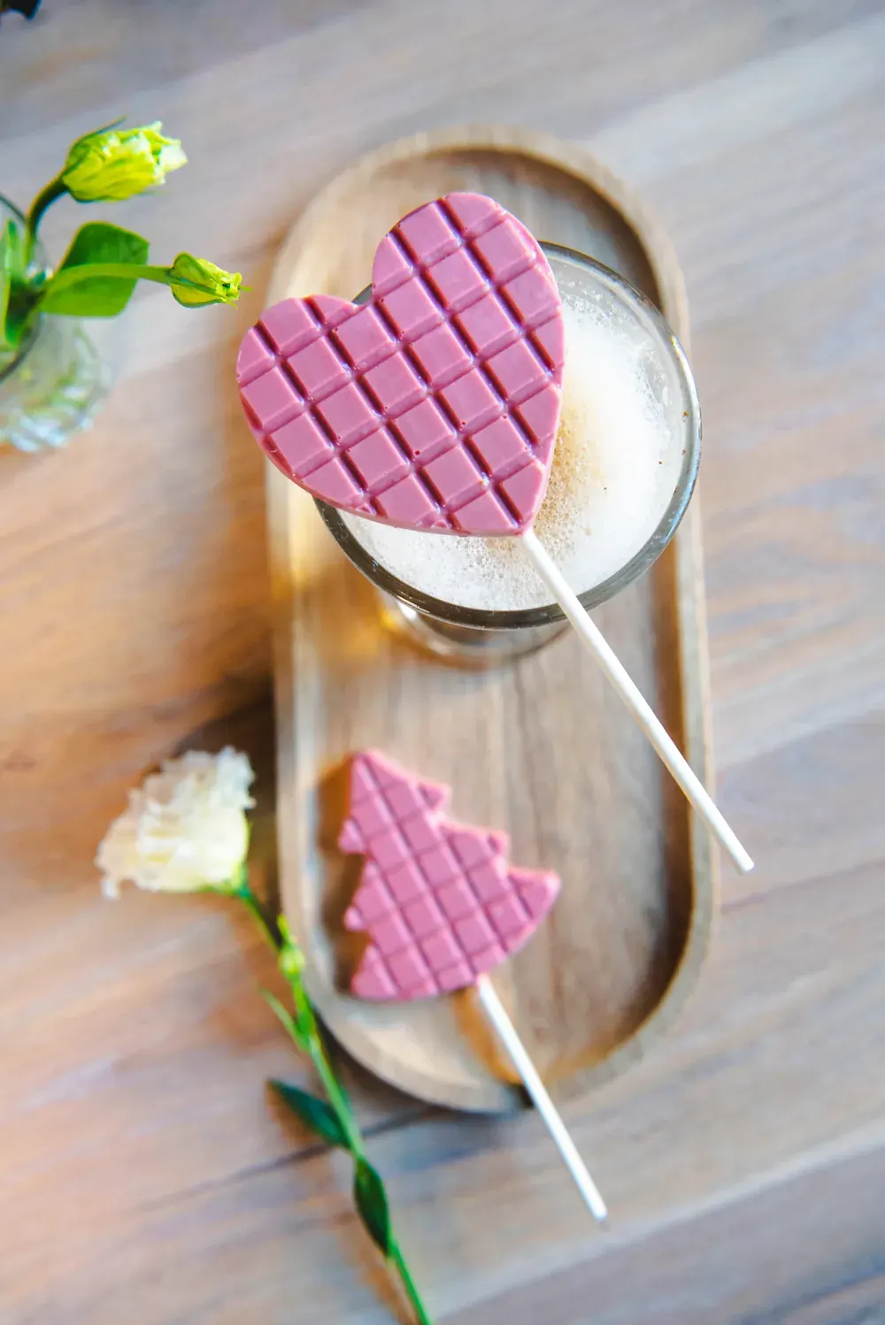 Acadele roz din ciocolată ruby Choco Toni în formă de inimă, pe un platou de lemn cu flori