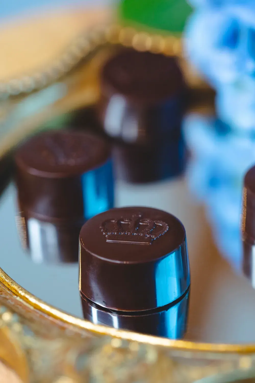 Bomboane rotunde de ciocolată neagră cu cremă de șampanie Choco Toni, reflectate într-o oglindă aurie
