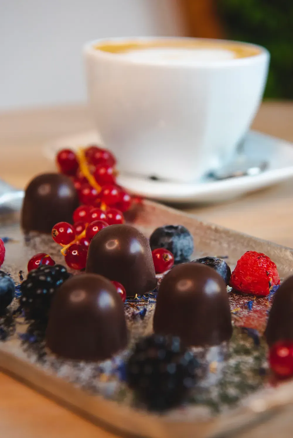 Bomboane de ciocolată neagră cu fructe de pădure Choco Toni lângă o cafea, cu zmeură și afine