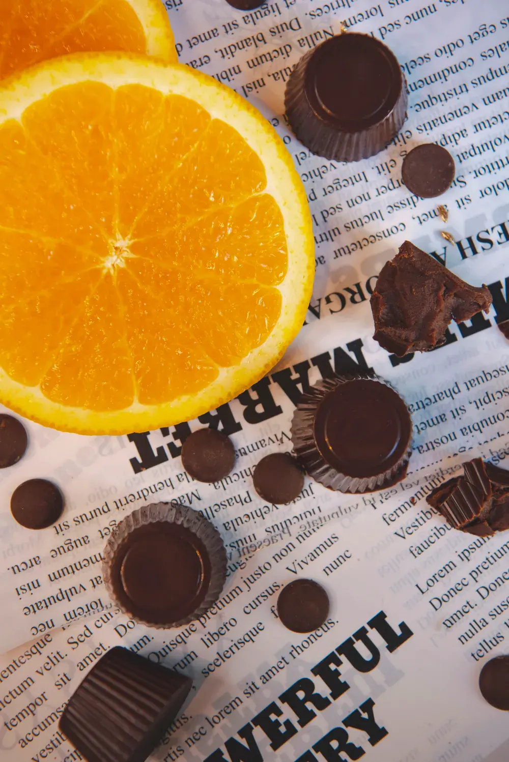 Bomboane de ciocolată neagră cu portocale Choco Toni și o jumătate de portocală, pe hârtie de ziar