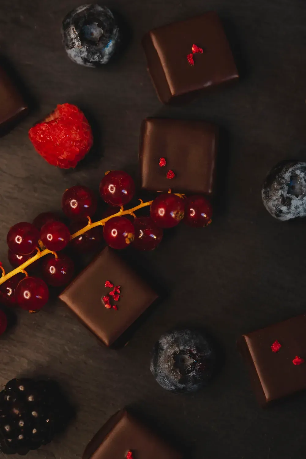 Bomboane de ciocolată neagră cu zmeură Choco Toni pe fundal închis, cu coacăze și mure
