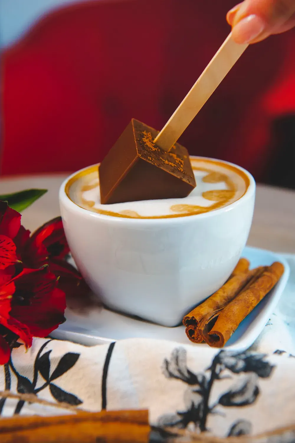 Ciocolată caldă cu lapte și scorțișoară Choco Toni înmuiată într-un cappuccino, cu bețișoare de scorțișoară