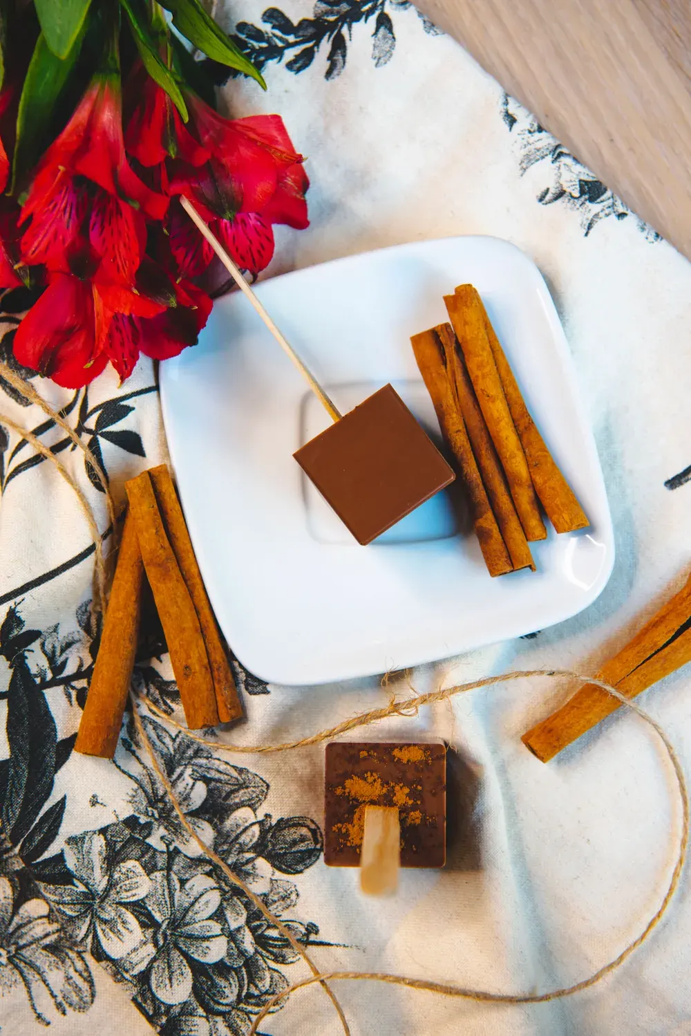 Ciocolată caldă cu lapte și scorțișoară Choco Toni pe o farfurie, cu bețișoare de scorțișoară și flori