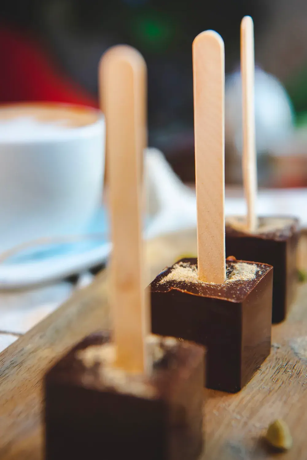 Cuburi de ciocolată caldă neagră cu cardamon Choco Toni pe băț, lângă o ceașcă de cafea