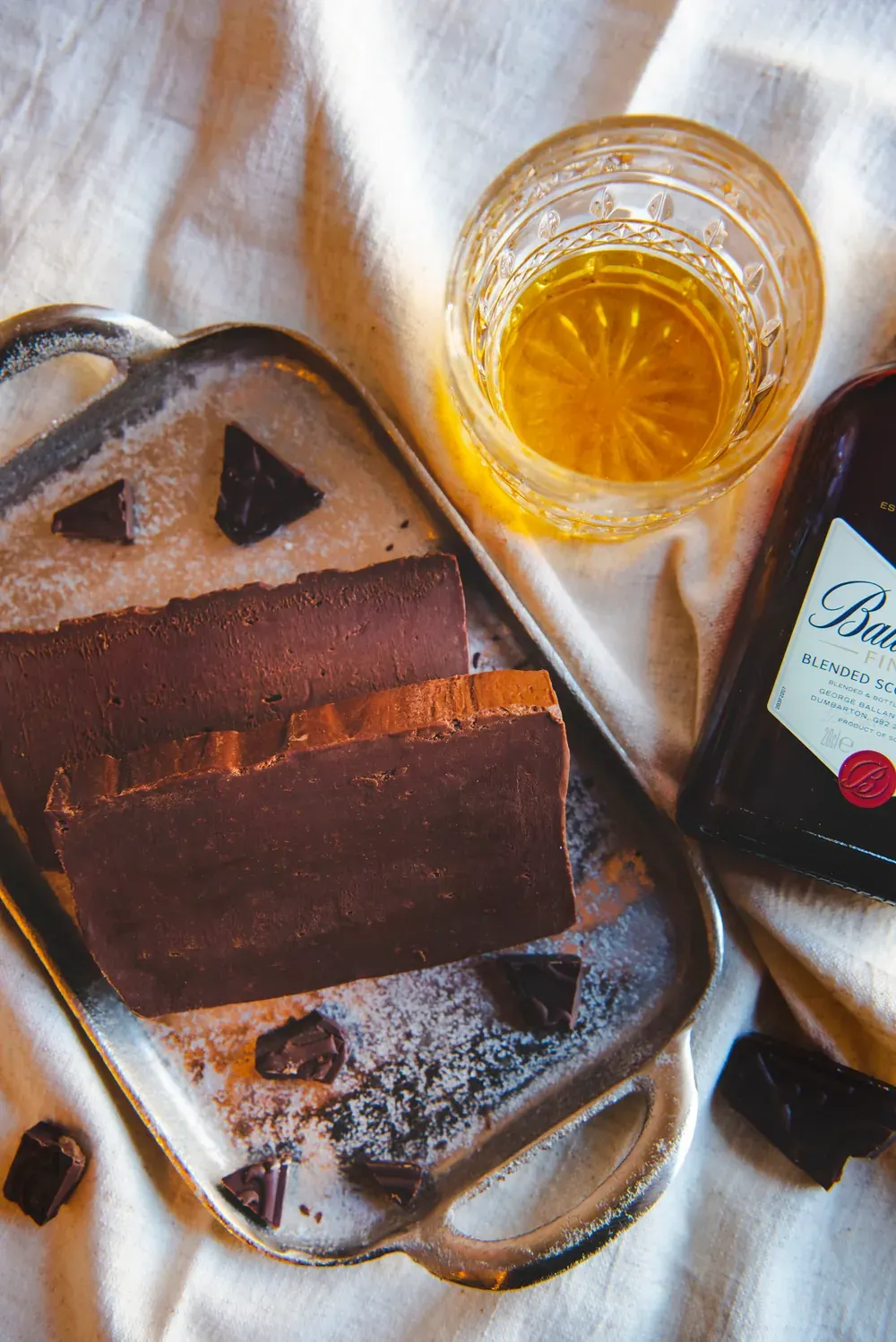 Fudge de ciocolată cu cremă de whiskey Choco Toni pe o tavă argintie, lângă un pahar de whisky