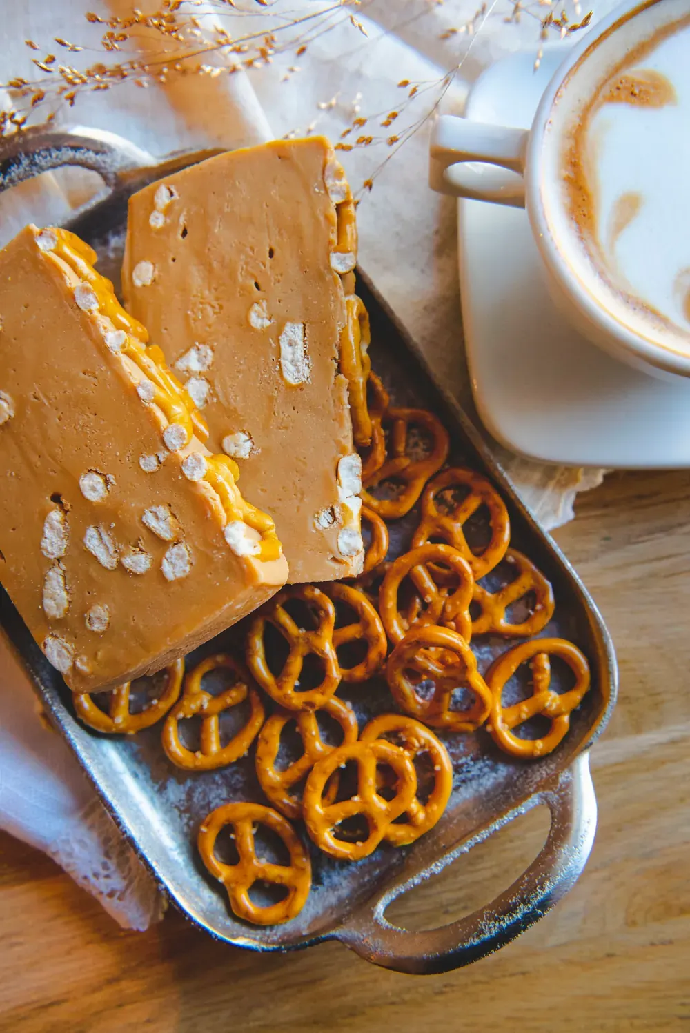 Fudge de ciocolată cu lapte, caramel și pretzels Choco Toni pe o tavă cu covrigei, lângă o cafea