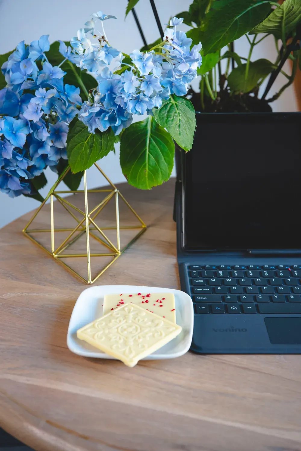 Tabletă de ciocolată albă Choco Toni pe o farfurioară, lângă un laptop și flori albastre