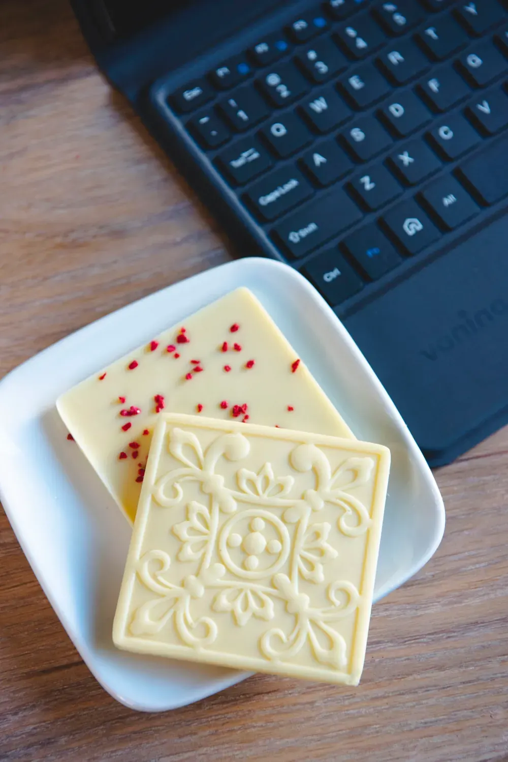 Tablete de ciocolată albă 34% Choco Toni cu model în relief și fulgi de zmeură, lângă o tastatură
