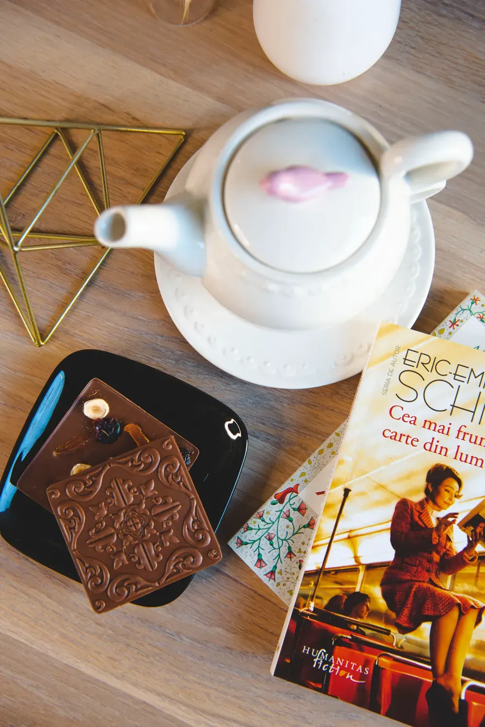 Tabletă de ciocolată cu lapte Choco Toni pe o farfurie neagră, lângă un ceainic și o carte