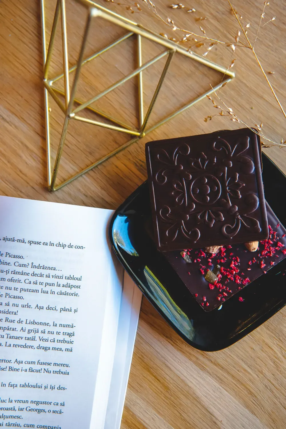 Tabletă de ciocolată neagră Choco Toni cu fulgi de zmeură, pe o farfurie neagră lângă o carte deschisă